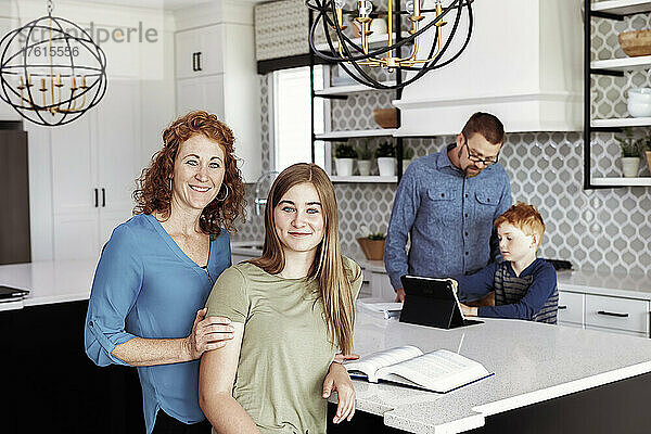 Vater hilft seinem kleinen Sohn bei den Hausaufgaben in der Küche  während eine Mutter und eine Tochter im Teenageralter in die Kamera schauen; Edmonton  Alberta  Kanada