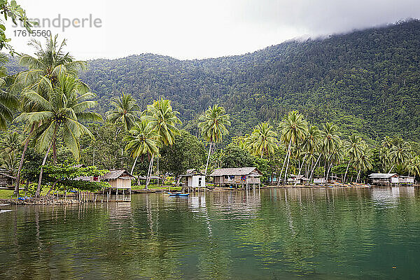 Dschungel und Küstendorf Siboma mit Hütten auf Stelzen  die sich im Wasser spiegeln  Insel Lababia  Huon-Golf; Siboma  Provinz Morobe  Papua-Neuguinea
