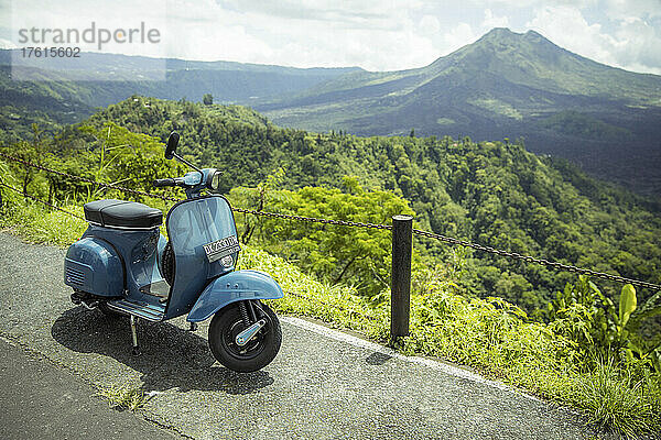 Am Straßenrand geparktes Moped an einem Aussichtspunkt mit Blick auf den Mount Batur (Vulkan Kintamani) in South Batur bei bewölktem Himmel und üppiger Vegetation; Kintamani  Bangli Regency  Bali  Indonesien