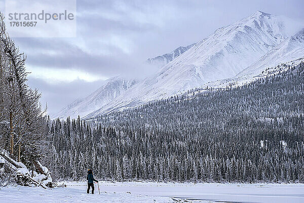 Frau steht am gefrorenen Ufer des Kathleen Lake und blickt auf die schneebedeckte Landschaft; Haines Junction  Yukon  Kanada