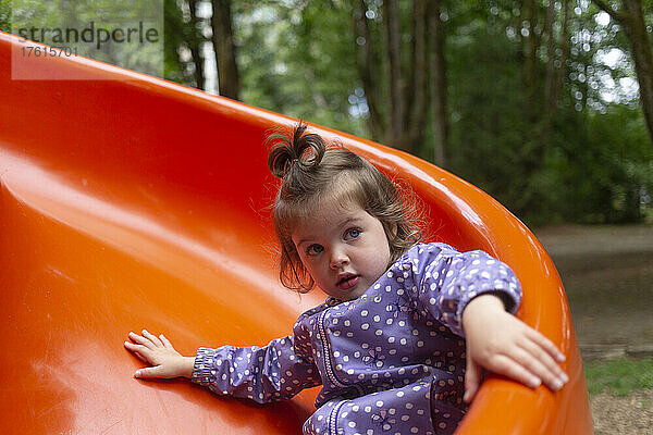 Vorschulmädchen auf einem Spielplatz  das eine rote Rutsche hinunterrutscht; North Vancouver  British Columbia  Kanada