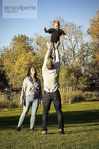 Junge Familie spielt an einem schönen Herbsttag zusammen im Park  wobei der Vater seinen kleinen Sohn hoch in die Luft wirft; St. Albert  Alberta  Kanada