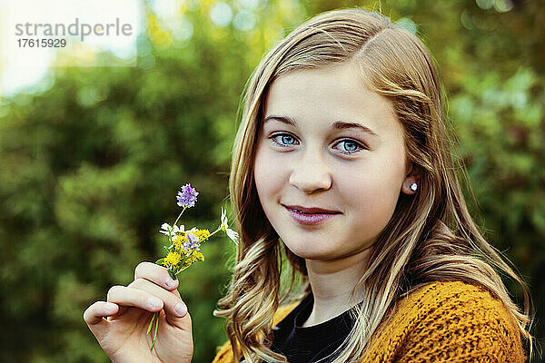 Teenager-Mädchen steht im Freien und hält ein kleines Bündel bunter Wildblumen in der Hand und schaut in die Kamera; Edmonton  Alberta  Kanada