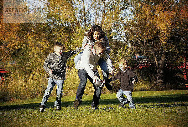Eine junge Familie mit zwei Jungen spielt Fußball in einem Stadtpark im Herbst; St. Albert  Alberta  Kanada