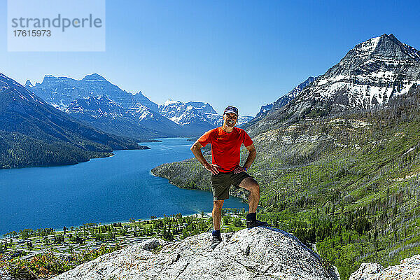 Ein männlicher Wanderer steht auf einer Felsklippe mit Bergen und einem See in der Ferne mit blauem Himmel  Waterton Lakes National Park; Waterton  Alberta  Kanada