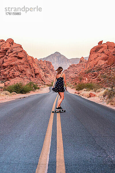 Eine Frau fährt mit dem Skateboard eine leere Wüstenstraße hinunter.