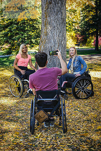 Junge querschnittsgelähmte Männer und Frauen in ihren Rollstühlen  die an einem schönen Herbsttag in einem Park Fotos mit einem Smartphone machen; Edmonton  Alberta  Kanada