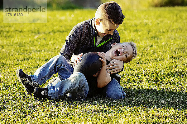 Zwei Brüder  die sich mit einem Fußball im Gras balgen; St. Albert  Alberta  Kanada