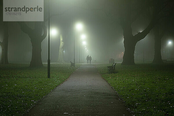 Silhouette von zwei Personen  die an einem nebligen Morgen in London Fields  Shoreditch  London  UK  spazieren gehen; London  England