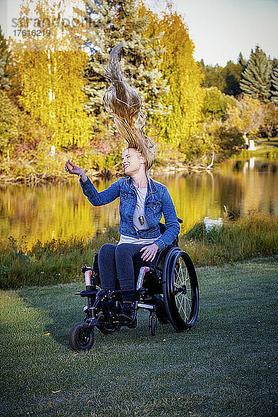 Junge querschnittsgelähmte Frau in ihrem Rollstuhl in einem Park an einem schönen Herbsttag  sie fühlt sich sorglos  ihr langes Haar weht nach oben; Edmonton  Alberta  Kanada