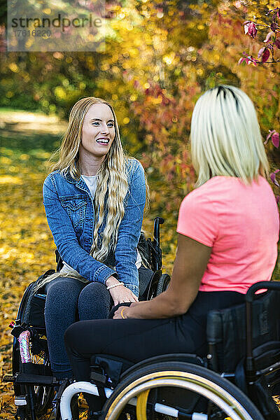 Zwei junge querschnittsgelähmte Frauen in ihren Rollstühlen besuchen an einem schönen Herbsttag gemeinsam einen Park; Edmonton  Alberta  Kanada