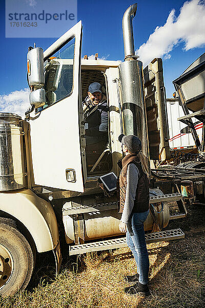 Älteres Ehepaar  das auf seiner Farm arbeitet und sich unterhält  wobei der Ehemann im Führerhaus eines Diesel-Lkw sitzt und die Ehefrau mit einem Tablet-Computer an der offenen Lkw-Tür steht; Alcomdale  Alberta  Kanada