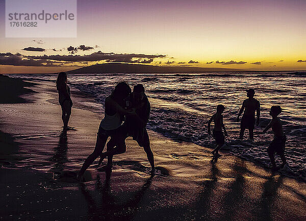 Silhouette von Touristen  die am nassen Strand des Ka'anapali Beach Resort spielen  mit einem dramatischen  farbenfrohen Sonnenuntergang am Horizont mit der Insel Lanai in der Ferne; Ka'anapali  Maui  Hawaii  Vereinigte Staaten von Amerika