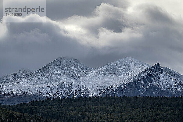 Winterliche Landschaft mit schneebedeckten Bergen unter dunklen Wolkenformationen und einem Wald im Vordergrund  in der Nähe der Stadt Whitehorse  Yukon; Yukon  Kanada