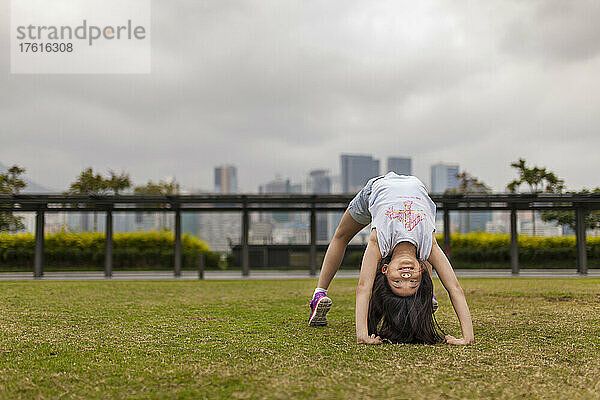 Junges Mädchen beim Turnen in einem Park mit der Skyline von Hongkong im Hintergrund; Hongkong  China