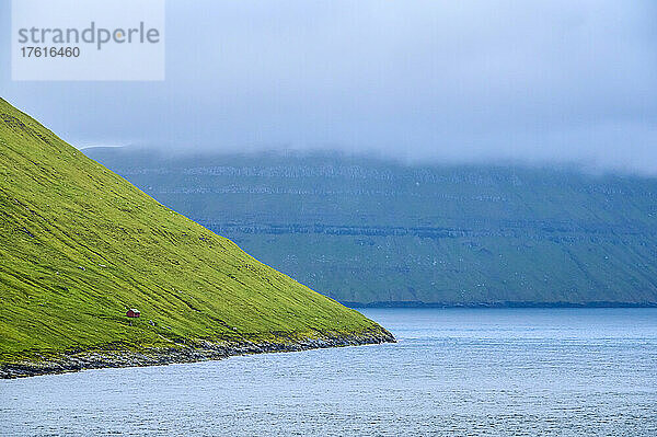 Hütte auf grasbewachsenem Berghang in der Nähe der Meeresküste  Blick von der aus Island kommenden Inselfähre MS Norröna  Fahrt durch die Insel der Färöer  ein autonomes dänisches Territorium; Färöer Inseln