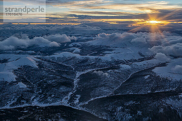 Luftaufnahme des Yukon im Winter mit der Sonne  die über den schneebedeckten Bergen aufgeht und eine surreale Landschaft unter sich entstehen lässt; Yukon  Kanada