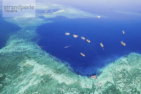 Luftaufnahme von Booten  die vor einer Insel im Komodo-Nationalpark vertäut sind  mit einem Pier  der in das umgebende türkisfarbene Wasser hineinragt; Ost-Nusa Tenggara  Kleine Sunda-Inseln  Indonesien