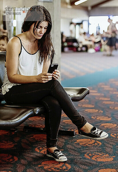 Eine Frau sitzt in einem Wartebereich eines Flughafens und benutzt ihr Smartphone; Kahului  Maui  Hawaii  Vereinigte Staaten von Amerika