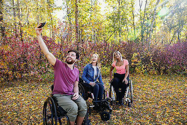 Junger querschnittsgelähmter Mann und Frau in ihren Rollstühlen  die an einem schönen Herbsttag in einem Park ein Selbstporträt mit einem Smartphone aufnehmen; Edmonton  Alberta  Kanada