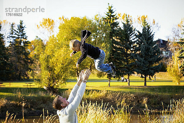 Vater spielt mit seinem kleinen Sohn in einem Park im Herbst und wirft ihn hoch in die Luft; St. Albert  Alberta  Kanada