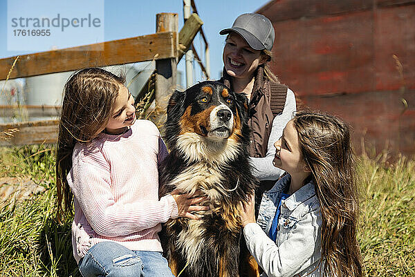 Mutter mit ihren beiden kleinen Töchtern  die ihren Hund auf der Familienfarm zärtlich behandeln; Alcomdale  Alberta  Kanada
