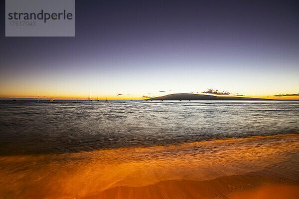 Silhouettierte Segelboote  die im ruhigen Wasser vor der Küste bei Sonnenuntergang vertäut sind  mit Blick auf die Insel Lanai von einem Strand in Lahaina; Lahaina  Maui  Hawaii  Vereinigte Staaten von Amerika