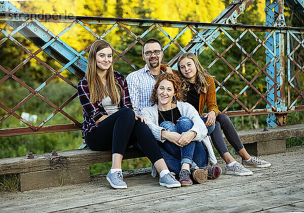 Außenporträt von Eltern mit zwei Töchtern im Teenageralter  die auf einer Brücke in einem Stadtpark im Herbst sitzen; Edmonton  Alberta  Kanada