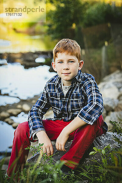 Porträt eines rothaarigen Jungen im Freien  der am Ufer eines Baches sitzt; Edmonton  Alberta  Kanada