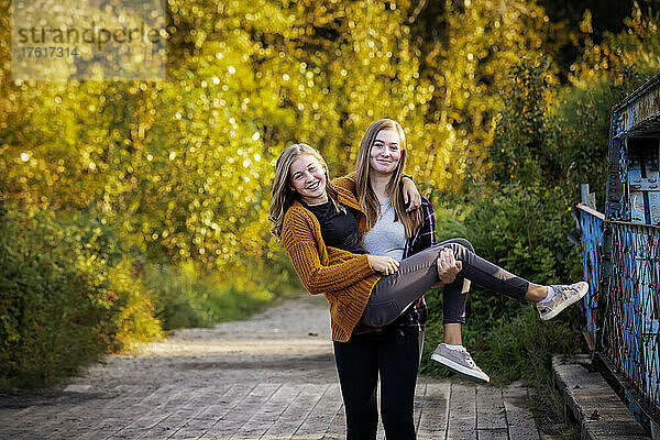 Zwei Schwestern  die zusammen in einem Park im Herbst albern sind  eine Schwester trägt die andere; Edmonton  Alberta  Kanada