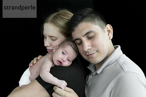 Familienporträt eines jungen Paares mit einem neugeborenen Mädchen vor einem schwarzen Hintergrund; Studio