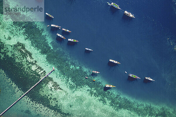 Blick von oben auf Boote  die vor einer Insel im Komodo-Nationalpark vertäut sind  mit einem Steg  der in das türkisfarbene Wasser hineinragt; Ost-Nusa Tenggara  Kleine Sunda-Inseln  Indonesien