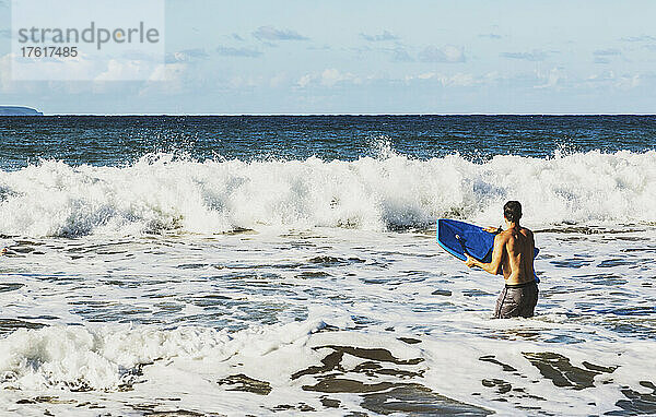 Blick von hinten auf einen Mann  der mit einem Bodyboard im Meer steht und darauf wartet  eine Welle am D. T. Fleming Beach zu erwischen; Kapalua  Maui  Hawaii  Vereinigte Staaten von Amerika