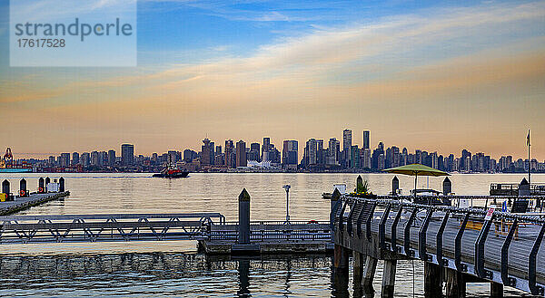 Blick auf die Skyline der Innenstadt von Vancouver und das Hafenviertel vom Lonsdale Quay aus  mit den Farben des Sonnenaufgangs  die sich im Wasser des Burrard Inlet spiegeln; Vancouver  British Columbia  Kanada