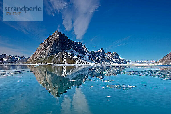 Ein zerklüftetes Gebirge  in dem sich der schmelzende Fjord spiegelt.