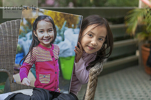 Junges Mädchen sitzt auf einem Stuhl und hält ein großes Foto von sich selbst; Hongkong  China