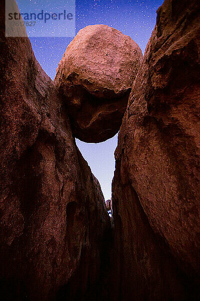 Dramatische Felsformation eines großen runden Felsblocks  der in einer Felsspalte unter einem sternenklaren Nachthimmel ruht  Joshua Tree National Park; Kalifornien  Vereinigte Staaten von Amerika