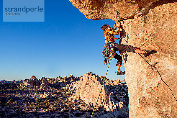 Ein Kletterer nimmt bei Sonnenuntergang einen Überhang über dem Hidden Valley im Joshua Tree National Park in Angriff.