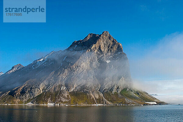 Wolken und Nebel an den zerklüfteten Bergen mit dem Fjord darunter.