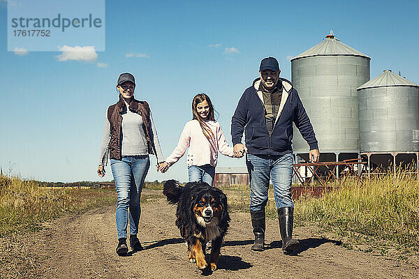 Eltern und ihre kleine Tochter gehen auf einem unbefestigten Weg mit ihrem Hund auf ihrer Familienfarm spazieren; Alcomdale  Alberta  Kanada