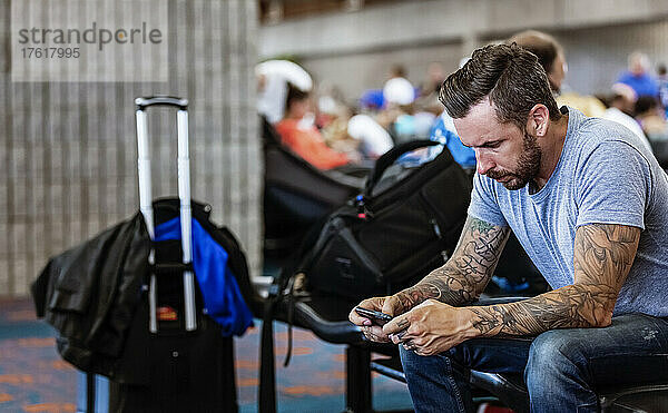 Ein Mann sitzt in einem Wartebereich eines Flughafens und benutzt sein Smartphone; Kahului  Maui  Hawaii  Vereinigte Staaten von Amerika