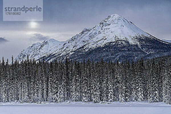 Schneebedeckte Berglandschaft in der Nähe des Tagish Lake im Winter mit Sonne  die beginnt  durch die Wolken zu schauen; Tagish  Yukon  Kanada