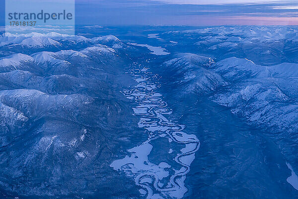 Luftaufnahme des Yukon im Winter mit einem rosafarbenen Sonnenaufgang über den blauen  schneebedeckten Bergen  die eine surreale Landschaft unter sich schaffen; Yukon  Kanada