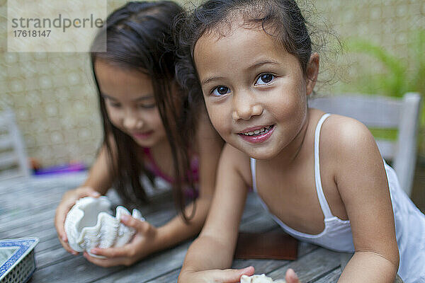 Junge Schwestern spielen mit Muscheln an einem Terrassentisch; Hongkong  China