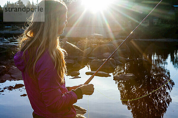 Eine junge Frau beim Fliegenfischen bei Sonnenuntergang.
