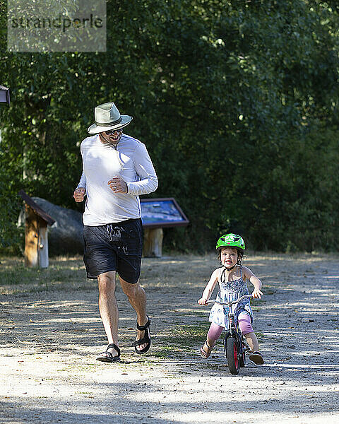 Vater läuft neben seiner kleinen Tochter  die ein Segelflugzeug fährt; British Columbia  Kanada