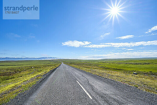 Weite  leere Straße im Sommer mit strahlend blauem Himmel über der Sonne; Austurland  Nordregion  Island