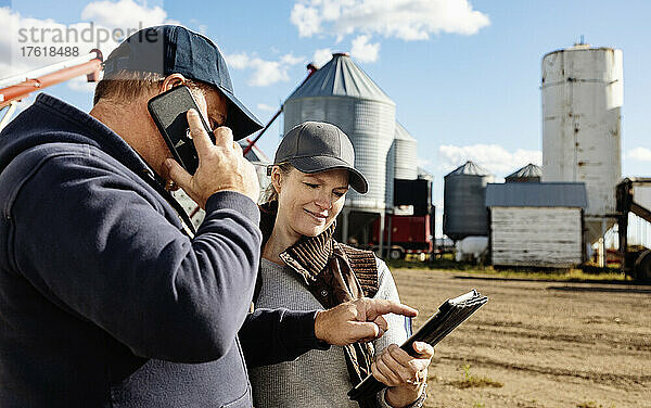 Älteres Ehepaar bei der Arbeit auf dem Bauernhof  das vor seinem Getreidespeicher steht  während es einen Tablet-Computer konsultiert und mit einem Mobiltelefon spricht; Alcomdale  Alberta  Kanada