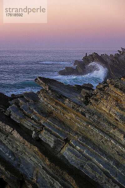 Rosa glühender Sonnenuntergangshimmel über dem Atlantik und den zerklüfteten Felsen an der Küste von Praia Baleal; Peniche  Oeste  Portugal