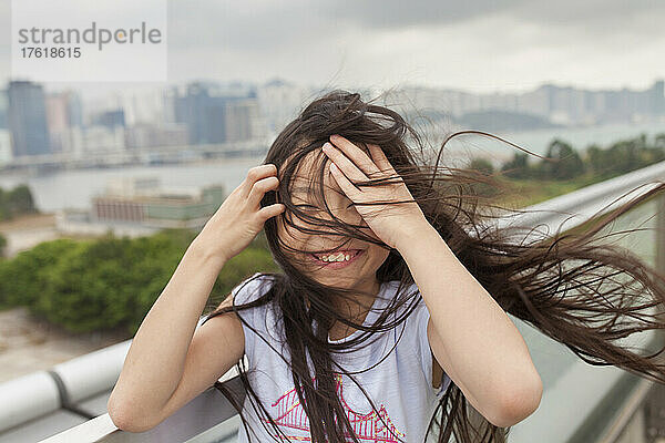 Mädchen mit verwehtem Haar kichert  während sie sich die Haare aus dem Gesicht streicht; Hongkong  China